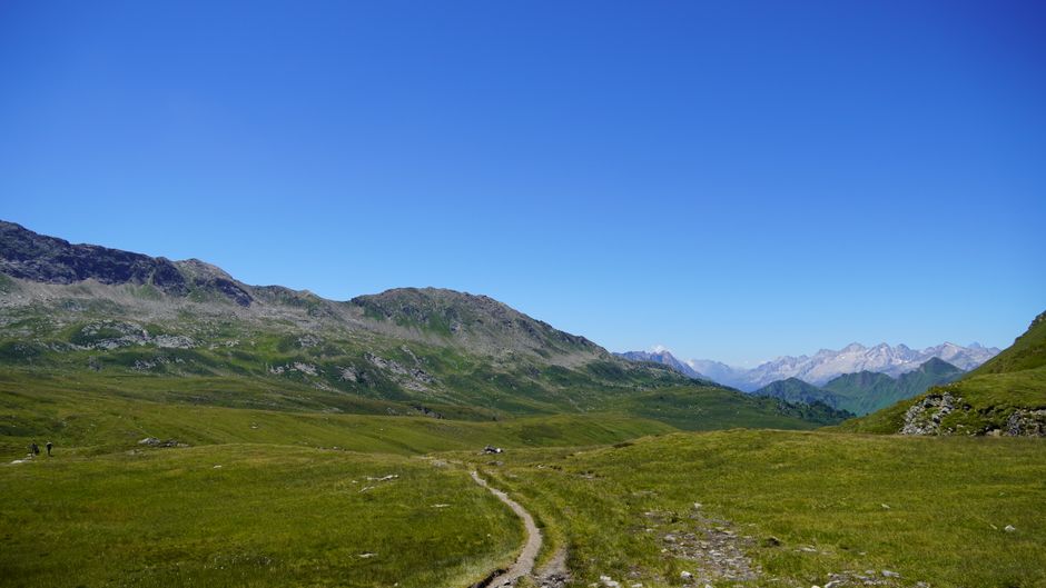 Discover a peaceful hiking trail leading through lush valleys and majestic mountains under a blue sky.